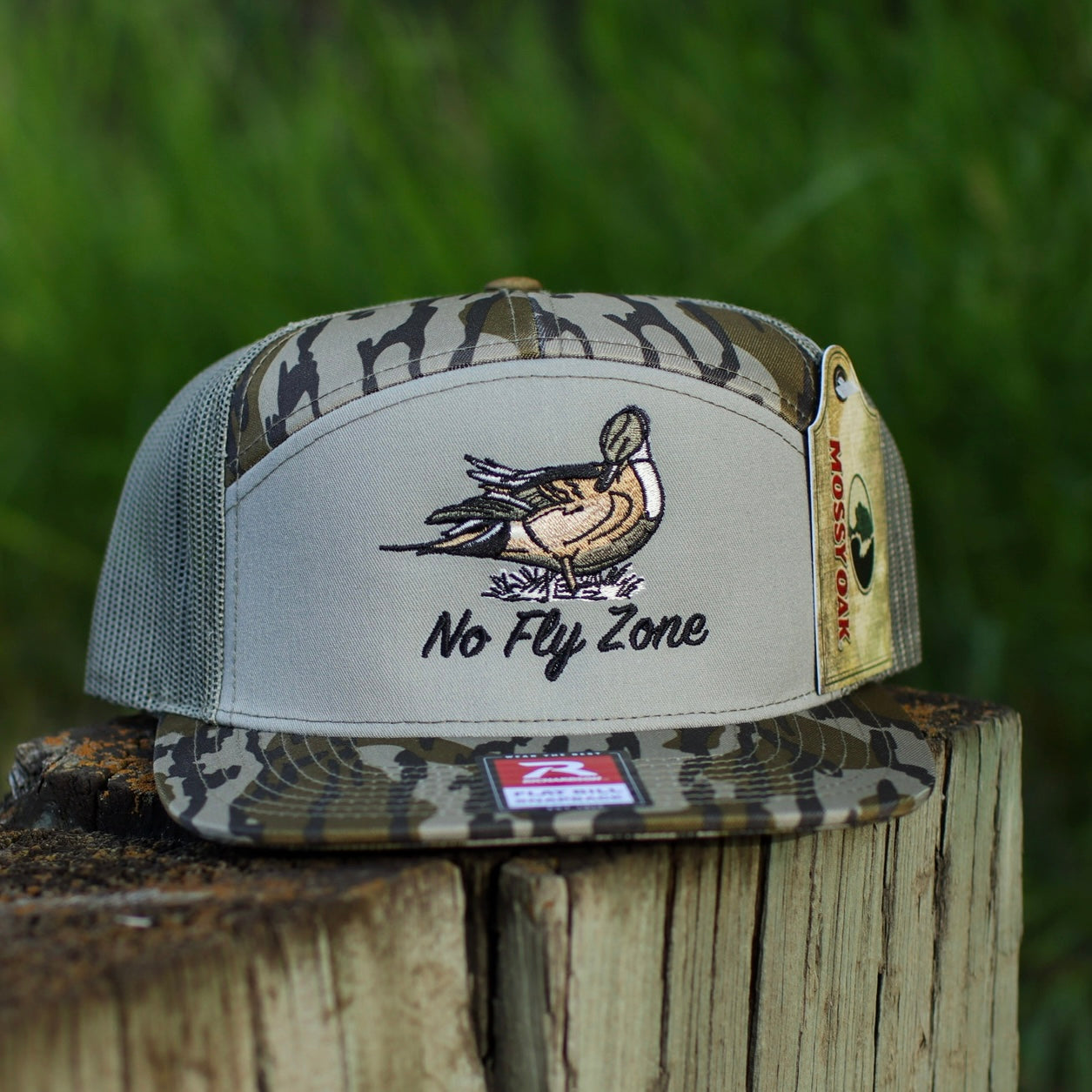 Camouflage cap with duck design and 'No Fly Zone' text on a wooden post with grass background
