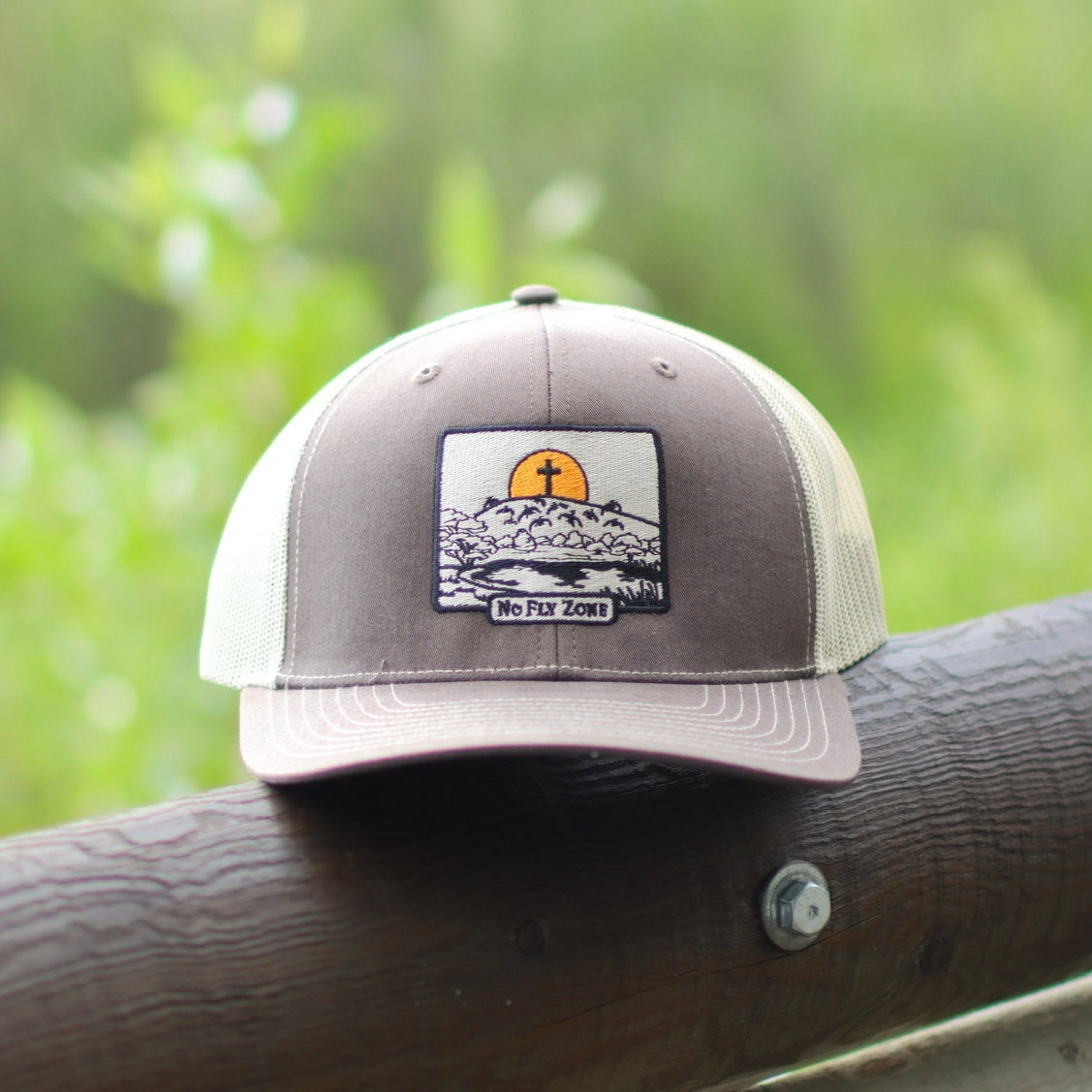 Gray and white cap with a patch of a cross on wooden post against a blurred green background