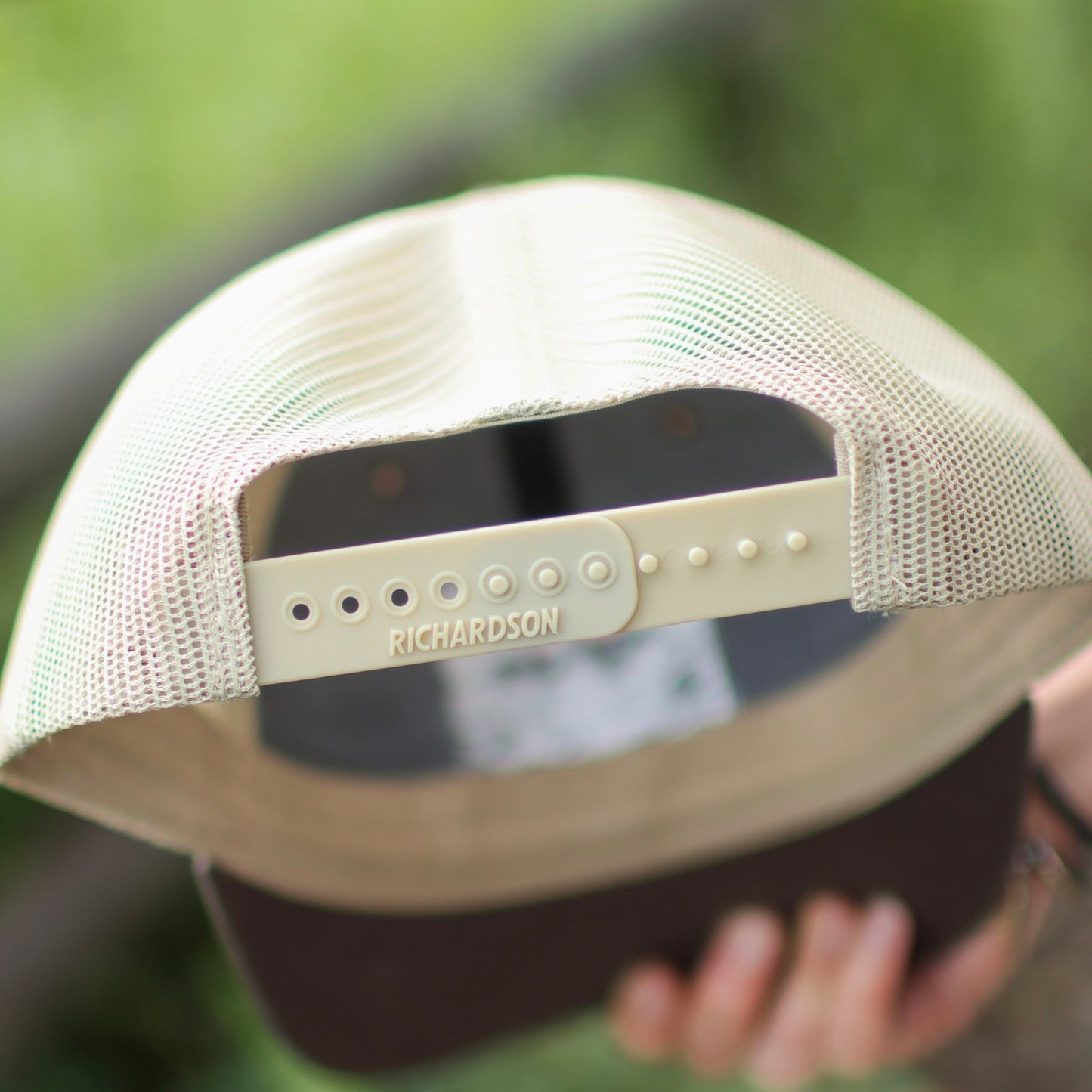 Beige mesh cap with Richardson logo held by a person against a blurred green background